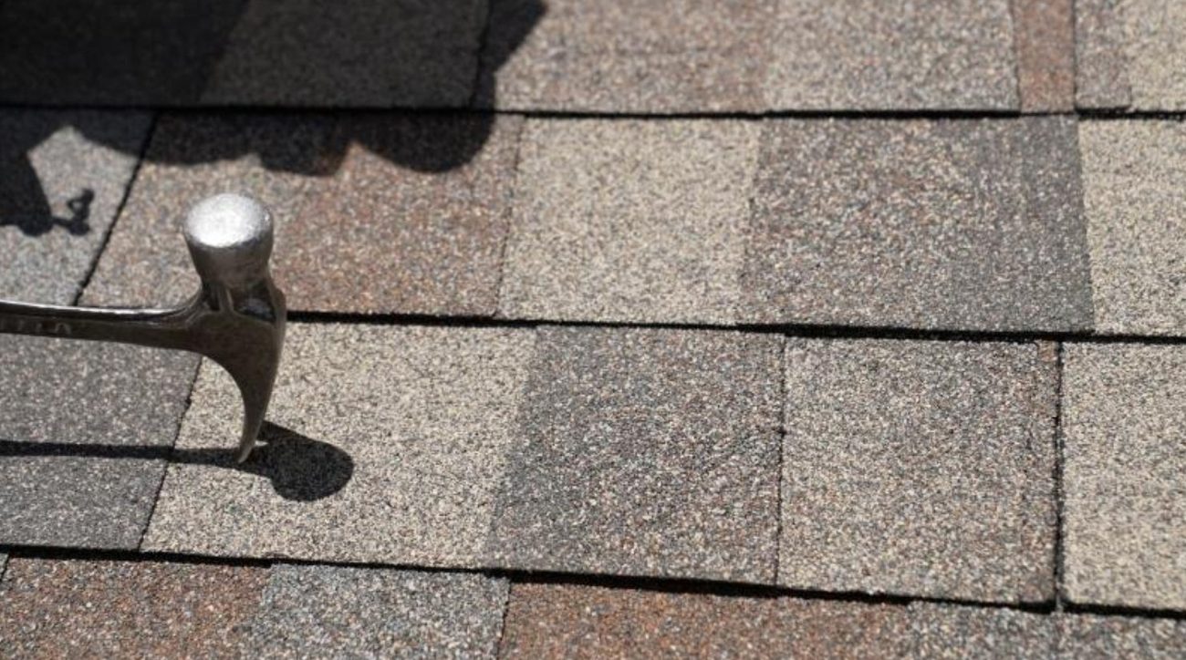 A hammer dragged across asphalt shingles to test granule adhesion